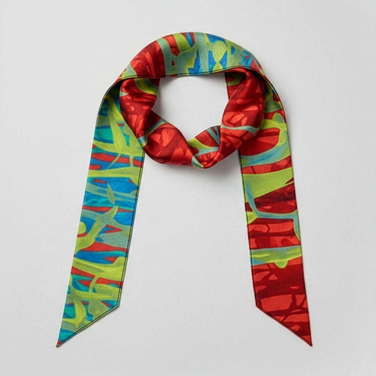 A silk scarf with a vibrant abstract pattern in red, green, and blue, styled in a loop on a light gray background.