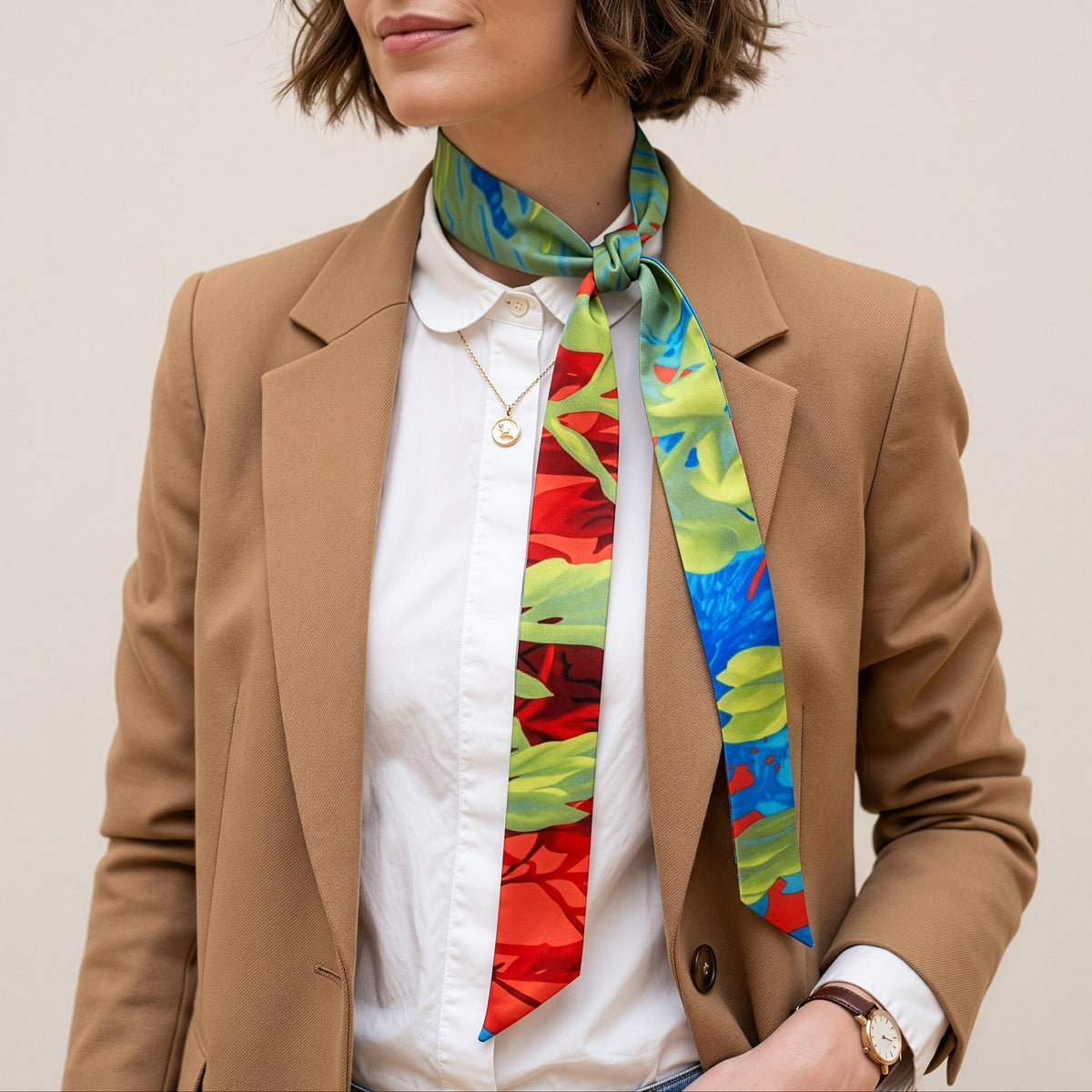 A woman wearing a tan blazer, white collared shirt, and a vibrant multicolor silk scarf tied around her neck, set against a plain beige background.