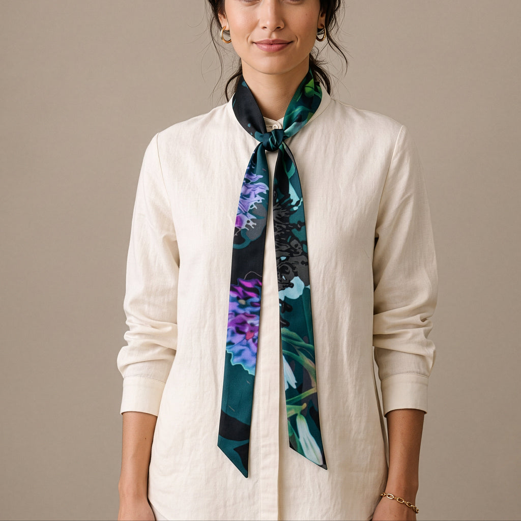 A woman wearing a cream-colored linen shirt and a dark teal silk scarf with a purple and blue floral pattern, standing against a solid beige background.