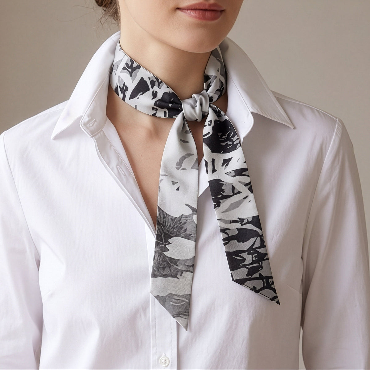A woman wearing a white button-up shirt and a black and white abstract floral silk neck scarf tied around her collar.