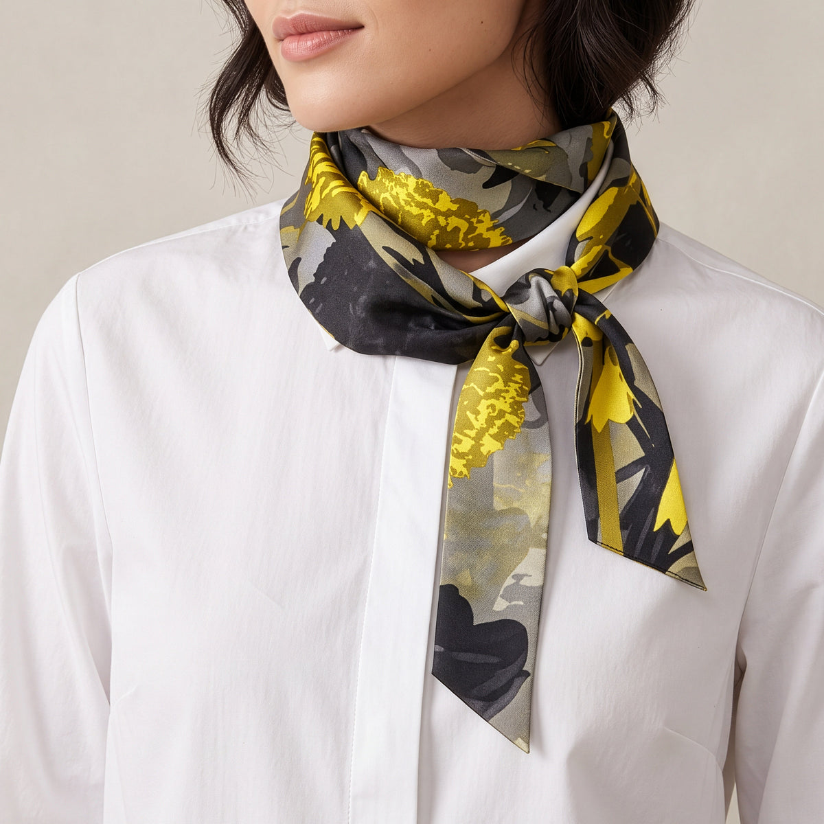 A woman wearing a white button-up shirt and a patterned silk scarf. The scarf features a bold yellow and black abstract floral design on a light gray background.