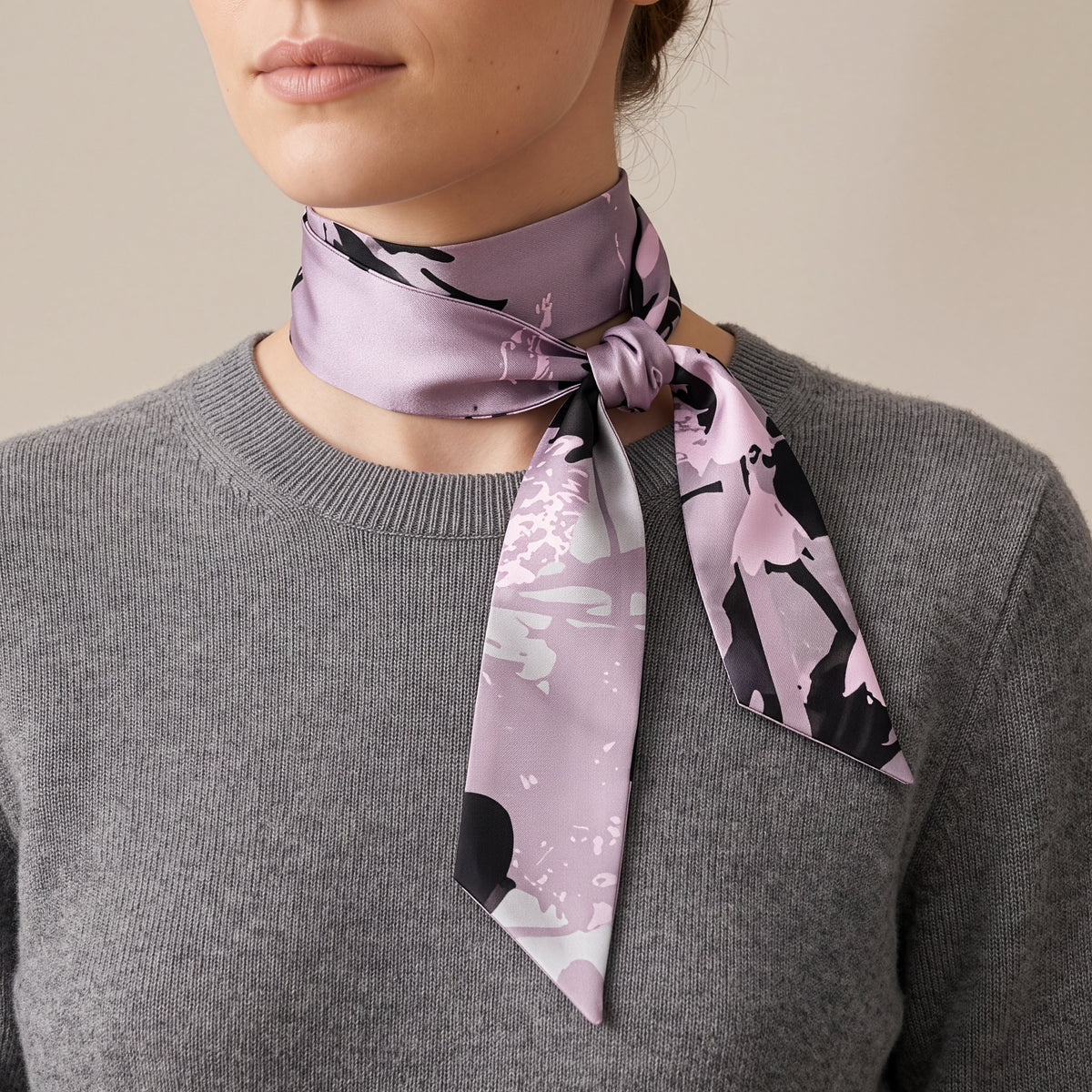 A close-up of a woman wearing a gray knit sweater and a lavender satin neck scarf with a black and white abstract pattern, tied in a knot at the collar.