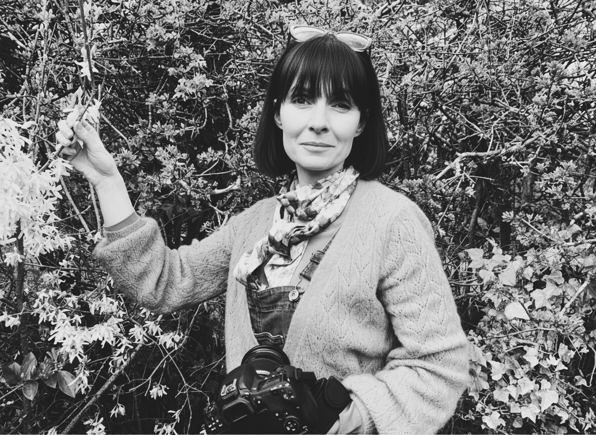 Black and white photo of a woman holding a plant in front of a bush
