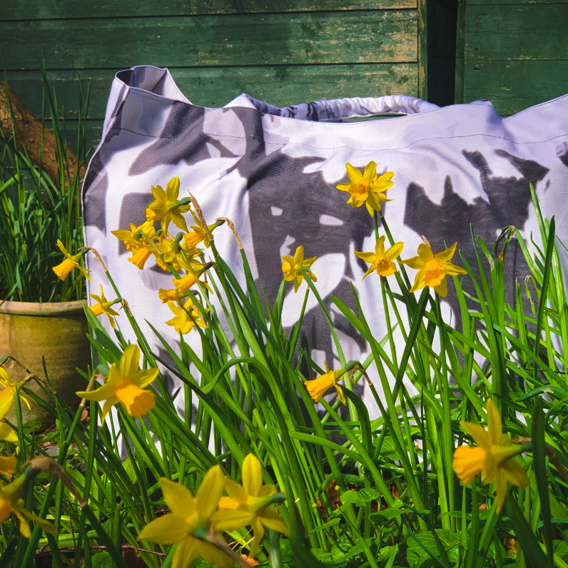 Tote bag with cow print in a garden setting with yellow flowers