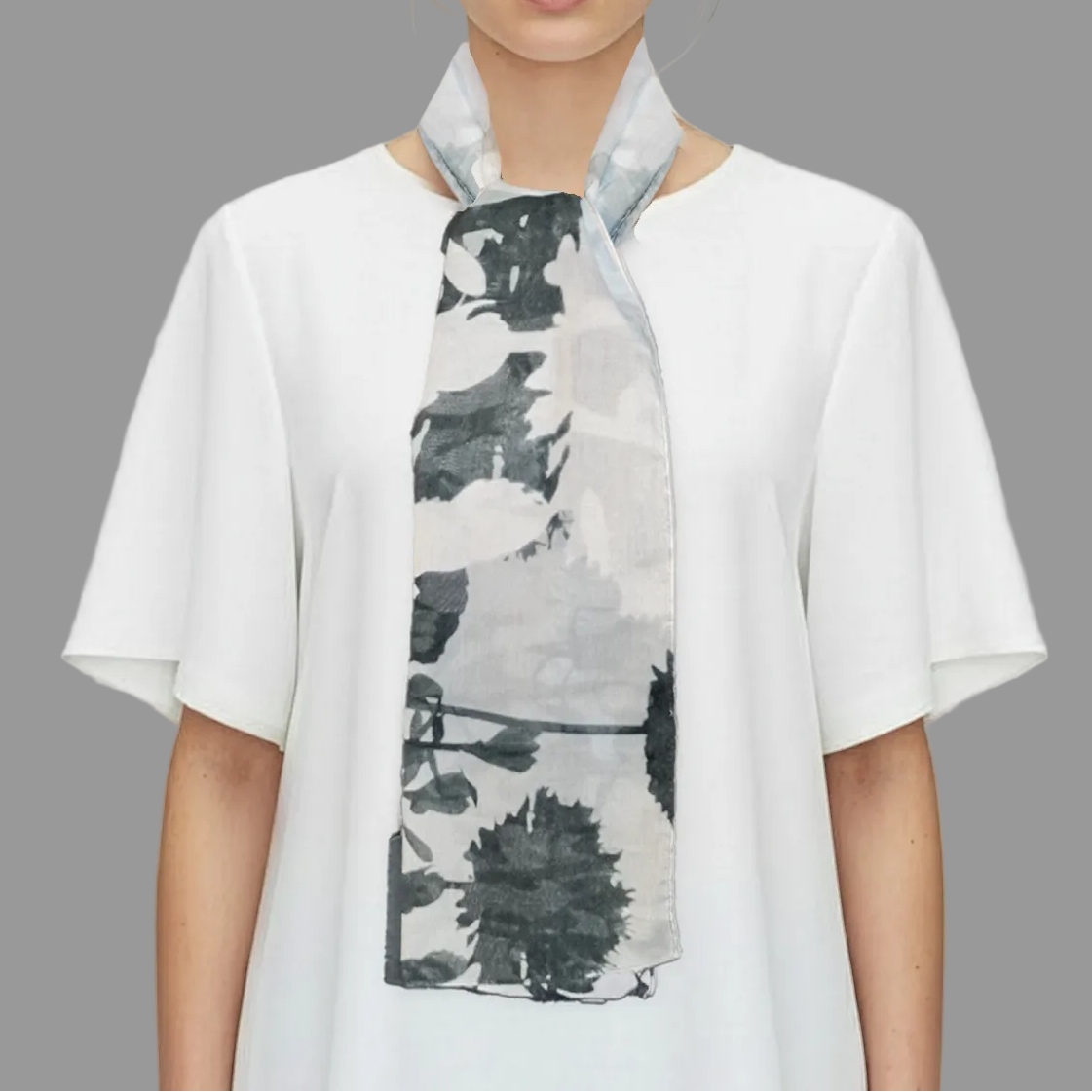 Woman wearing a white shirt with a black and gray patterned scarf on a gray background