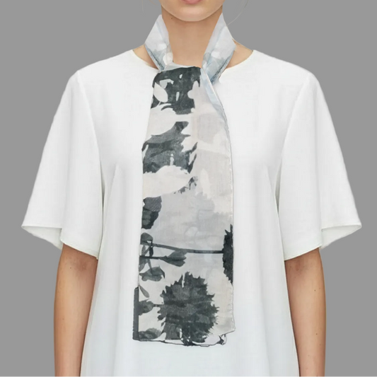 Woman wearing a white shirt with a black and gray patterned scarf on a gray background