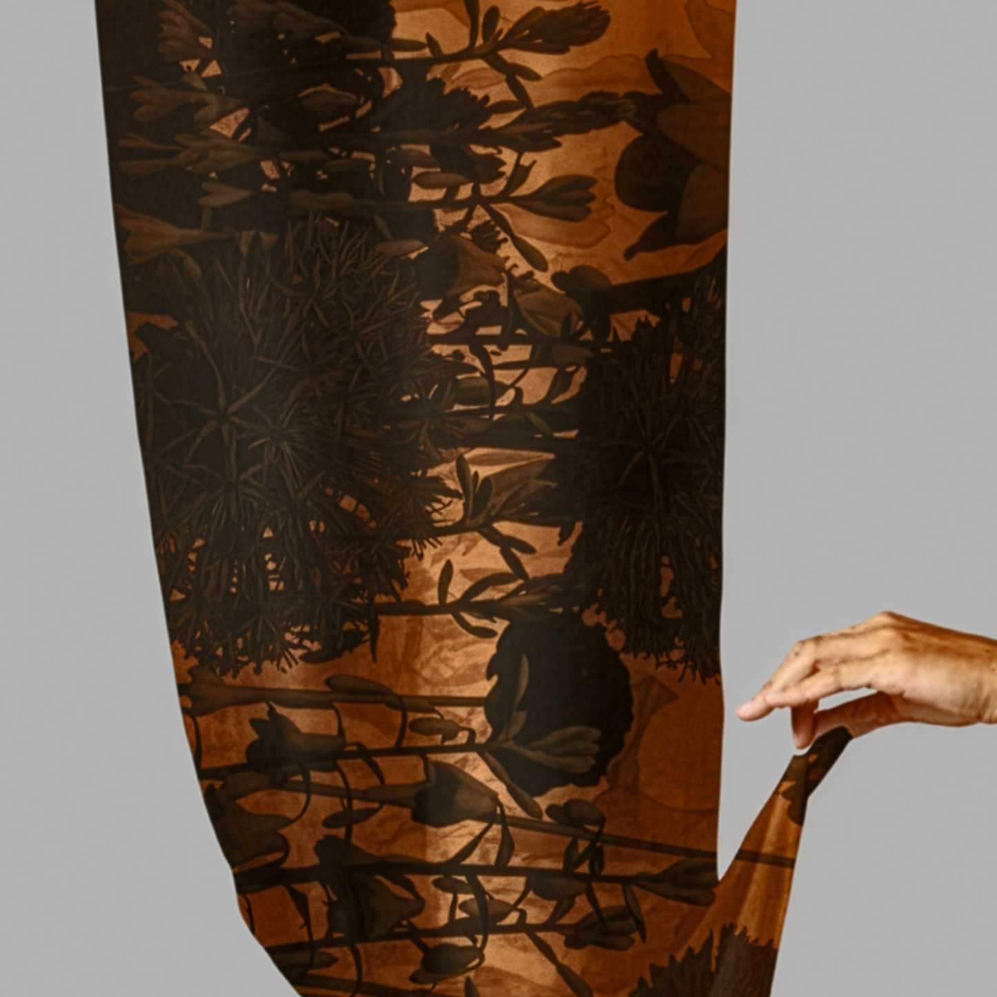Person holding a long, patterned fabric with a dark design on a gray background